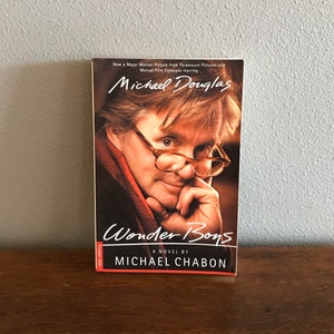 May include: A book cover featuring a close-up photo of Michael Douglas, the actor, with the title "Wonder Boys" and the author's name, Michael Chabon, printed below. The book cover is red, white, and black.