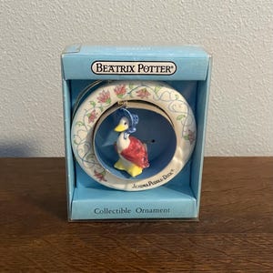 May include: A white porcelain ornament featuring Jemima Puddle-Duck from Beatrix Potter's children's books. The ornament is in a box with a blue background and the text "Beatrix Potter" and "Collectible Ornament".
