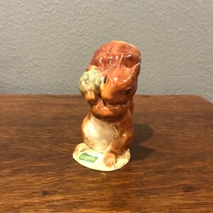 May include: A brown and white ceramic squirrel figurine holding a green acorn. The figurine is standing on a green base with the word "Beswick" written on it.