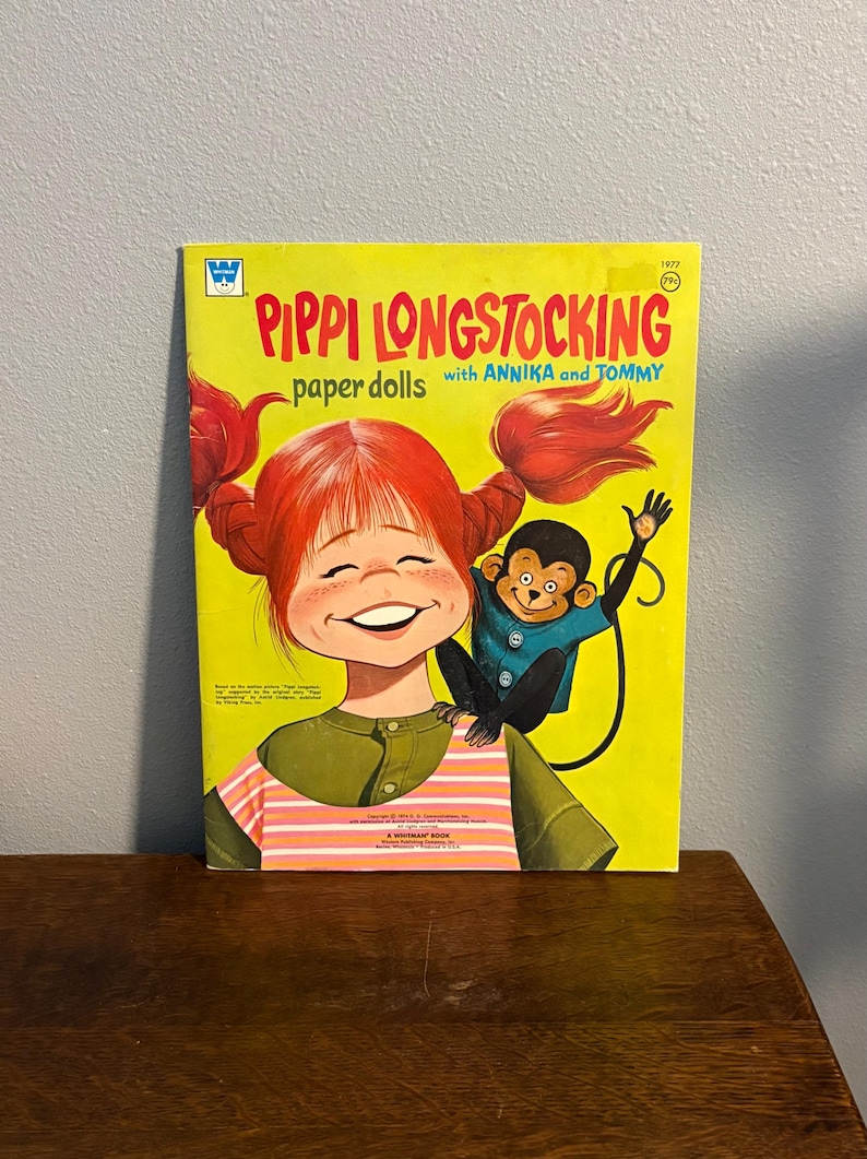 May include: A vintage Pippi Longstocking paper dolls book with a bright yellow cover. The illustration features a red-haired character with pigtails and a small monkey on their shoulder. The text reads Pippi Longstocking paper dolls with Annika and Tommy.