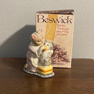 Puede incluir: Una figurita de cerámica de dos gatos, Tabitha Twitchit y Miss Moppet, de la serie de Beatrix Potter. La figurita está hecha por Beswick y presenta a los gatos sentados juntos, con Tabitha sosteniendo un trozo de pan.