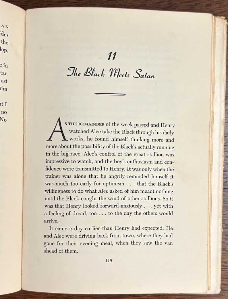 May include: Open book page with text. The title "The Black Meets Satan" is displayed in elegant script above a horizontal line. The text is in black ink on aged, off-white paper, with a large initial letter.