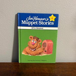 May include: A hardback book titled Jim Henson's Muppet Stories 4: Off to Storyland. The cover features a blue top section with a yellow star and a green bottom section. Fozzie Bear is illustrated in the centre next to a red radio.