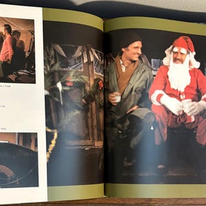 Op de afbeelding: Dubbele pagina uit een boek. Rechts een man in een kerstmanpak, zittend naast een man in een groene jas. Op de linkerpagina een gezin in een kamer en een man met een paard.