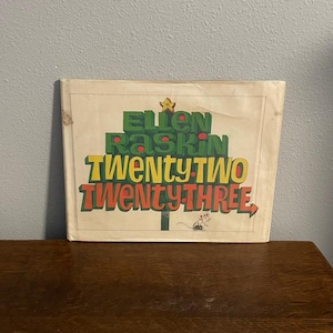 May include: A vintage book cover with the text "Ellen Raskin Twenty Two Twenty Three" in green, yellow, and red. The design is in the shape of a Christmas tree with a star on top and a small mouse illustration.
