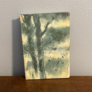 May include: A vintage book cover with a watercolor illustration of a tree and a field. The illustration is in shades of blue and green.