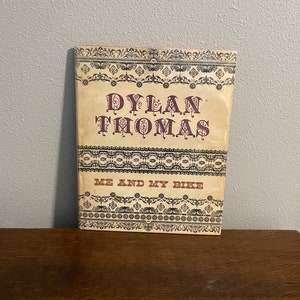 May include: A vintage book cover with a cream background and black and white decorative borders. The title "Dylan Thomas" is in large, purple letters. The subtitle "Me and My Bike" is in smaller, brown letters.