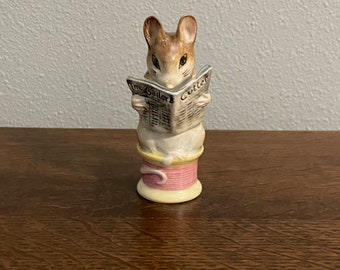 May include: A ceramic figurine of a mouse reading a newspaper titled "The Gaillora Cutter". The mouse is sitting on a spool of thread.