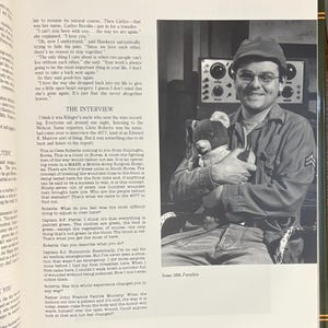 Op de afbeelding: Een zwart-witfoto van een man in militair uniform, met een bril en een pet, die een teddybeer vasthoudt. De man glimlacht. De afbeelding komt uit een boek, met tekst op de omliggende pagina's.