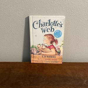May include: A copy of "Charlotte's Web" by E.B. White. The book cover shows a girl with a pig and other animals. The title is in a decorative font, with the author and illustrator's names below. A children's classic.