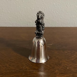 May include: A silver bell with a badger figurine on top. The bell is polished and shiny.