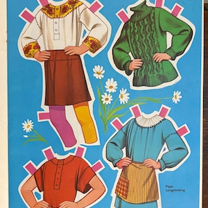 May include: A paper doll sheet featuring Pippi Longstocking with four outfits: a white blouse with floral embroidery and a brown skirt, a green cable-knit sweater, a red short-sleeved shirt, and a blue dress with a striped apron and white collar.