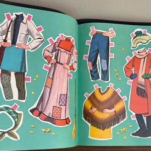 May include: A paper doll book page featuring various outfits including a white jacket with a blue skirt, a striped dress with patches, blue jeans, a yellow and brown poncho, a red coat with a scarf, a plaid headscarf, and a knit hat.
