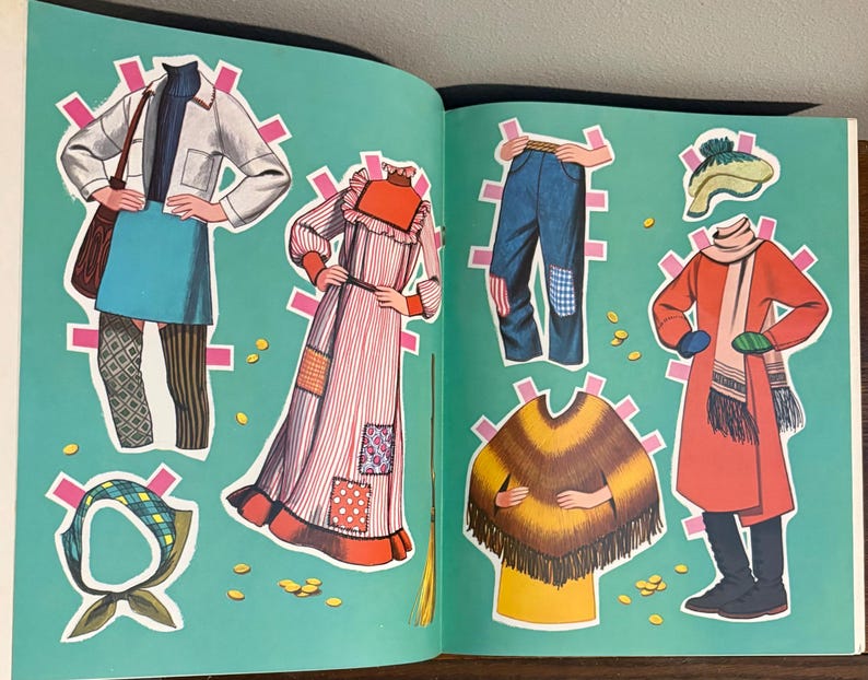 May include: A paper doll book page featuring various outfits including a white jacket with a blue skirt, a striped dress with patches, blue jeans, a yellow and brown poncho, a red coat with a scarf, a plaid headscarf, and a knit hat.