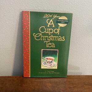 May include: A hardcover book titled "A Cup of Christmas Tea" with a green cover and gold lettering. The book has a red floral border and an image of a teacup. An "Autographed Copy" sticker is on the cover.