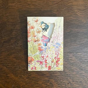 May include: A vintage greeting card featuring a whimsical illustration of a figure in a garden. The card has a die-cut window revealing a woman in a bonnet and dress amidst colorful flowers. The card is rectangular and has a light-colored border.