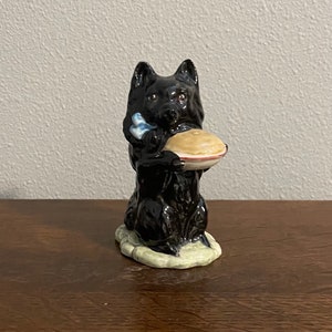 以下が含まれることがあります： パイを持っている犬の黒いセラミック製置物。犬は緑色の台座に座っています。