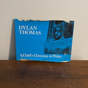 May include: A blue book cover with the title "Dylan Thomas A Child's Christmas in Wales" with illustrations by Fritz Eichenberg.