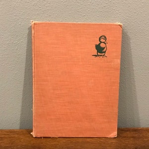 May include: A vintage children's book with a pink linen cover and a black and green illustration of a duckling on the front.