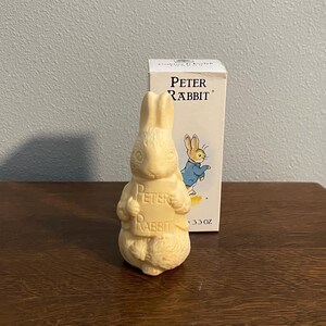 Puede incluir: Una figurita de cerámica blanca de Peter Rabbit sosteniendo un cartel que dice "Peter Rabbit". La figurita pesa 3,3 onzas y está al lado de una caja con la misma imagen.
