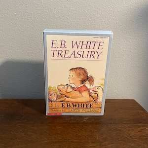 Pode incluir: Um livro de capa dura intitulado "E.B. White Treasury" com uma borda azul clara. A ilustração da capa apresenta uma menina ruiva, um porco, uma ovelha e um pato. O nome do autor, E.B. White, e do ilustrador, Garth Williams, também são visíveis.