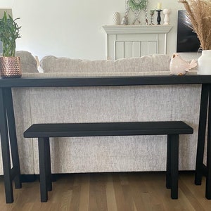 May include: A black console table with a matching black bench. The table has a simple, modern design with a rectangular top and two A-frame legs. The bench is also rectangular with a simple design and two legs.