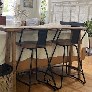 May include: Two black metal bar stools with wooden seats and a natural wood counter top.