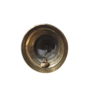 Puede incluir: Vista superior de una peque&ntilde;a campana de color lat&oacute;n. La campana tiene forma redondeada con un interior oscuro y un peque&ntilde;o badajo visible en la parte inferior. La campana est&aacute; sobre un fondo blanco.