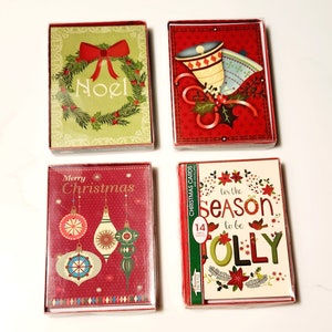 May include: Four boxed Christmas card sets. One features a green wreath with a red bow and the word "Noel." Another has bells and holly on a red background. A third has ornaments and the words "Merry Christmas." The last says "tis the season to be jolly."