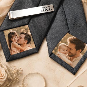 May include: Two black textured neckties featuring custom photo prints of a person with a child. A silver-toned metal tie bar is clipped onto one tie, engraved with the letters JKL in a black serif font. The fabric has a visible diagonal weave.