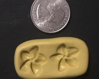 May include: A yellow silicone mold with two flower shapes. The mold is about the size of a quarter.