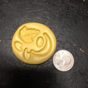 May include: A yellow silicone mold with a leaf and a curved shape. The mold is about the size of a US quarter.