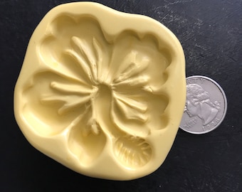 May include: A yellow silicone mold shaped like a hibiscus flower. The mold is about the size of a US quarter.