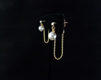 May include: A pair of gold chain earrings with a pearl drop on each side. The chain is connected to the pearl drop on one side and hangs down from the other side.