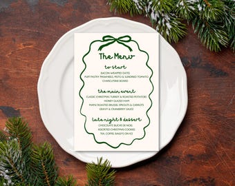 May include: A festive Christmas menu card on a white plate, featuring a green bow and decorative border. The menu lists starters, main courses like turkey and potatoes, and desserts such as Buche de Noel. The card is set on a wooden table with pine branches.