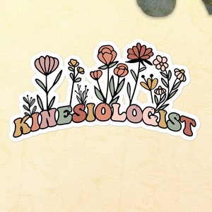 Può includere: Un adesivo con un design floreale colorato e la parola "KINESIOLOGIST" in un font retrò. L'adesivo è su uno sfondo giallo chiaro con coriandoli e verde.