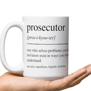 May include: White ceramic mug with a black and white definition of the word "prosecutor" printed on it. The definition reads: "[pros-i-kyoo-ter] one who solves problems you don't know exist in ways you don't understand. see also; superhero, legend, rockstar"