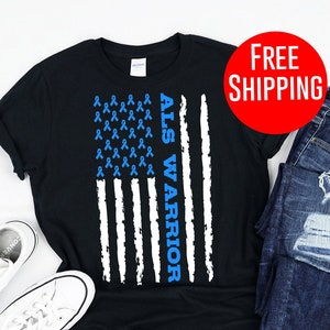 Peut inclure: T-shirt noir avec un motif de drapeau américain blanc et bleu. Le drapeau est composé de rubans bleus et les mots "ALS Warrior" sont écrits verticalement sur le côté droit du drapeau.