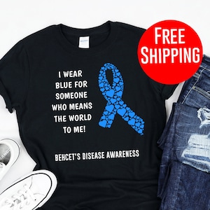 May include: Black t-shirt with a blue ribbon made of hearts and the text "I wear blue for someone who means the world to me! Behcet's Disease Awareness".