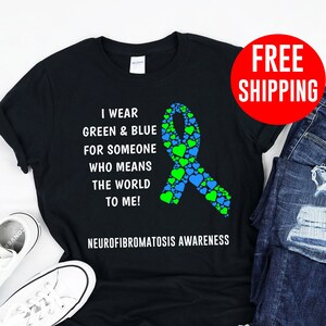 Könnte beinhalten: Schwarzes T-Shirt mit einem grünen und blauen Band aus Herzen. Der Text auf dem Shirt lautet "Ich trage Grün & Blau für jemanden, der die Welt für mich bedeutet! Neurofibromatose-Bewusstsein".