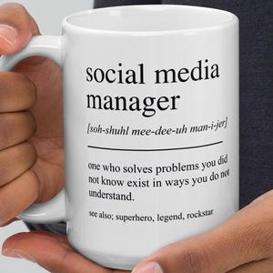 May include: White ceramic mug with the text "social media manager" and a definition. The definition includes the phonetic pronunciation and the phrase "one who solves problems you did not know exist in ways you do not understand."