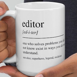 May include: White ceramic mug with the word "editor" printed in black, along with its pronunciation and a definition. The definition reads: "one who solves problems you did not know exist in ways you don't understand." The mug also lists "superhero, legend, rockstar."