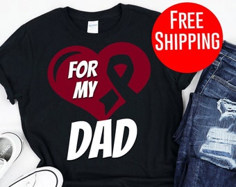 Può includere: T-shirt nero con un cuore rosso e un design a nastro, con la scritta bianca "FOR MY DAD". L'immagine include anche un paio di scarpe da ginnastica bianche e jeans blu.