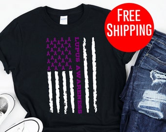 May include: Black t-shirt with a distressed American flag design featuring purple awareness ribbons and the text "Lupus Awareness." The shirt is paired with blue jeans and white trainers.