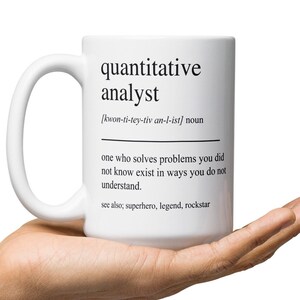 May include: White ceramic mug with the definition of "quantitative analyst" printed in black. The definition includes the pronunciation, and the phrase "one who solves problems you did not know exist in ways you do not understand."