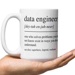 Op de afbeelding: Een witte keramische mok met een zwart ontwerp met de tekst "data engineer [dey-tuh en-juh-neer] one who solves problems you'd not know exist in ways you don't understand. see also; superhero, legend, rockstar"