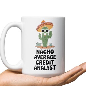 May include: White ceramic coffee mug with a cactus wearing a sombrero and sunglasses. The text on the mug reads "Nacho Average Credit Analyst".