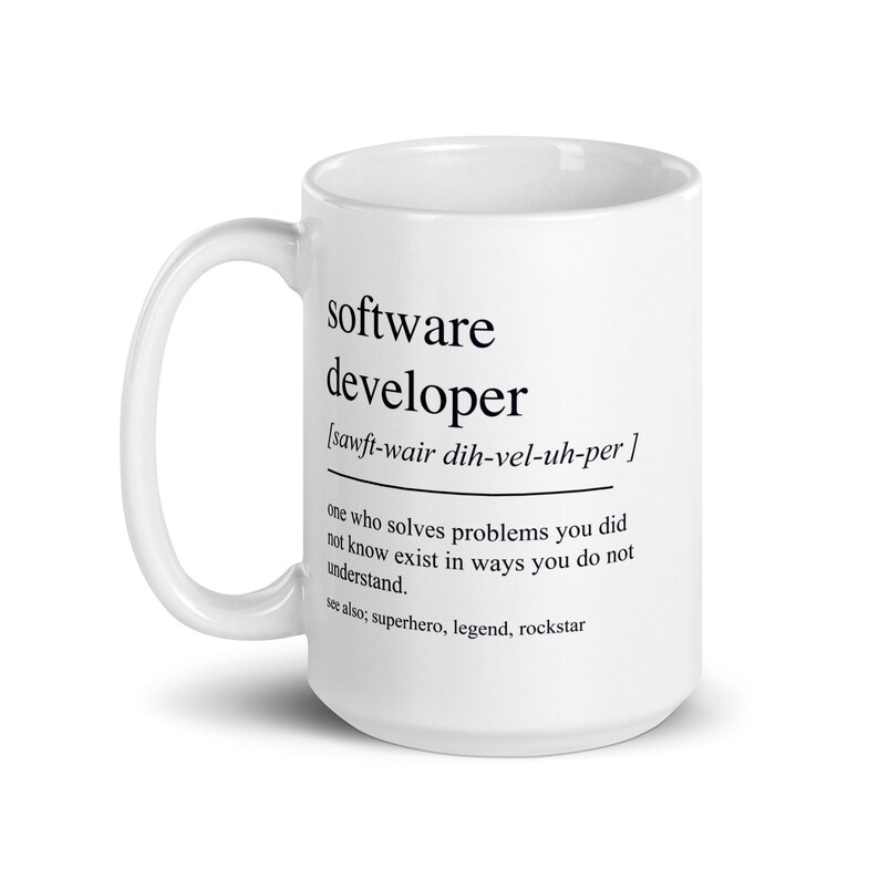 Op de afbeelding: Een witte keramische mok met een zwarte afbeelding waarop staat "Softwareontwikkelaar [sawft-wair dih-vel-uh-per] iemand die problemen oplost waarvan je niet wist dat ze bestonden, en dat op een manier die je niet begrijpt. zie ook: superheld, legende, rockster"
