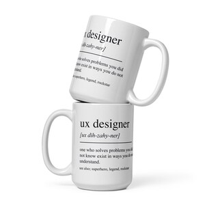 Op de afbeelding: Twee witte keramische mokken die op elkaar zijn gestapeld. De bovenste mok leest "designer" met een fonetische uitspraak en een definitie. De onderste mok leest "ux designer" met een fonetische uitspraak en een definitie.