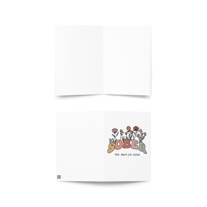 May include: A white greeting card, folded in half, with the word "SOBER" in colorful, retro-style lettering. The card is decorated with floral illustrations and the text "Est. April 27, 2023".